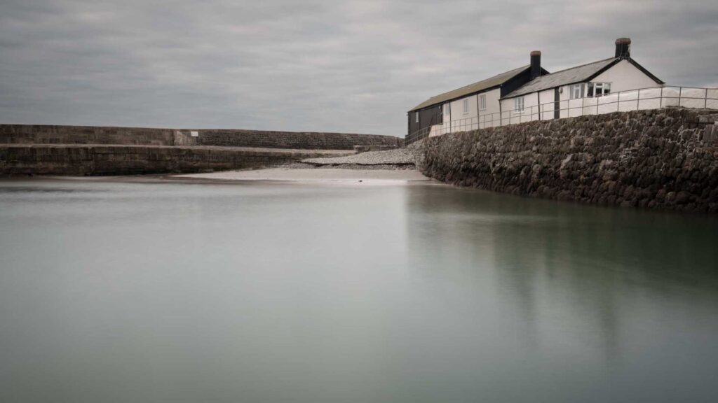 Harbour inlet with stone walls and waterside buildings, water smoothed by long exposure.