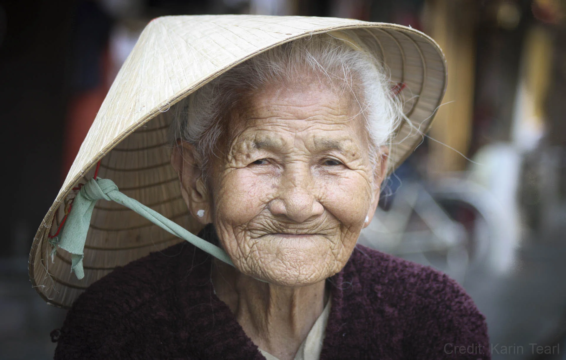 Elderly woman wearing a conical hat, smiling.