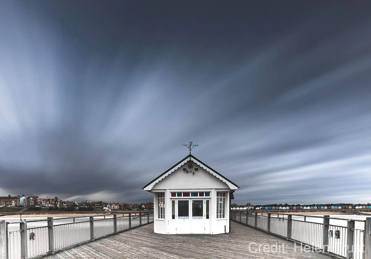Wooden pier with a white pavilion under a dramatic, cloudy sky.