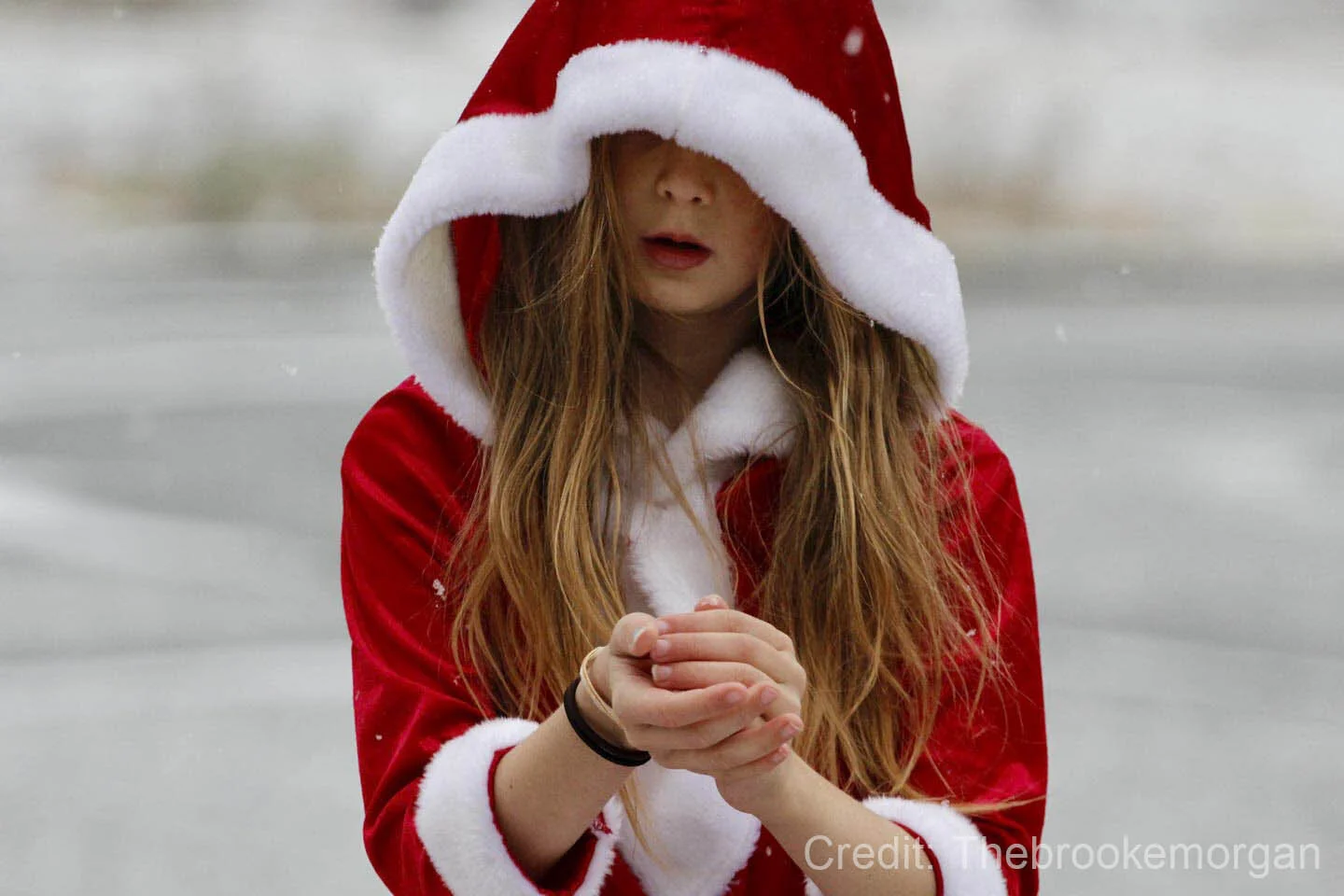 Young girl in a red and white hooded coat with hands clasped together, standing in a snowy landscape.