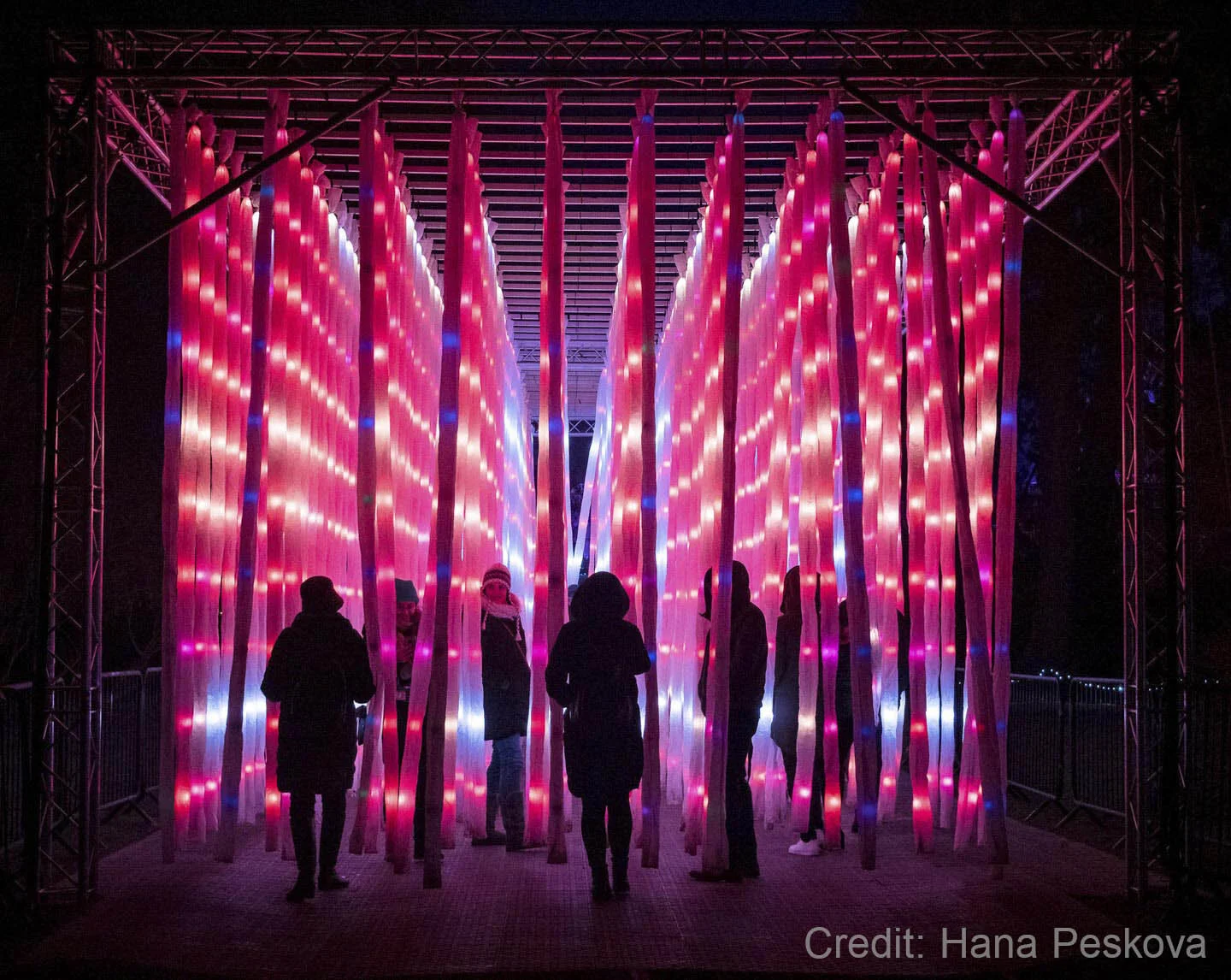 People walking through an art installation with glowing pink and blue vertical strips.
