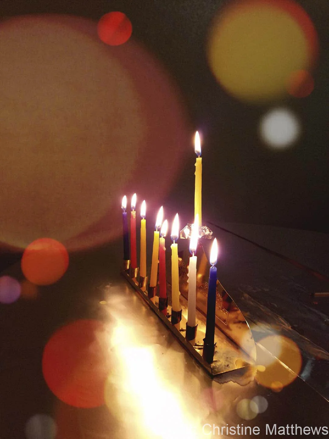 Lit menorah with nine candles on a reflective surface, surrounded by bokeh lights.
