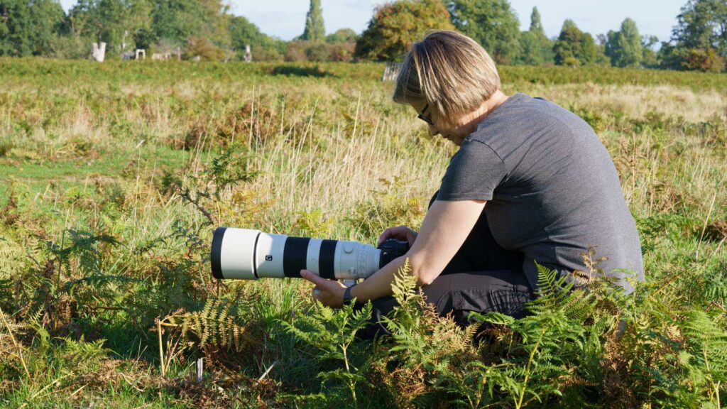 Crouched among bracken, Connie Kinley checks camera settings on a Sony A1 II fitted with the FE 200–600mm G OSS.