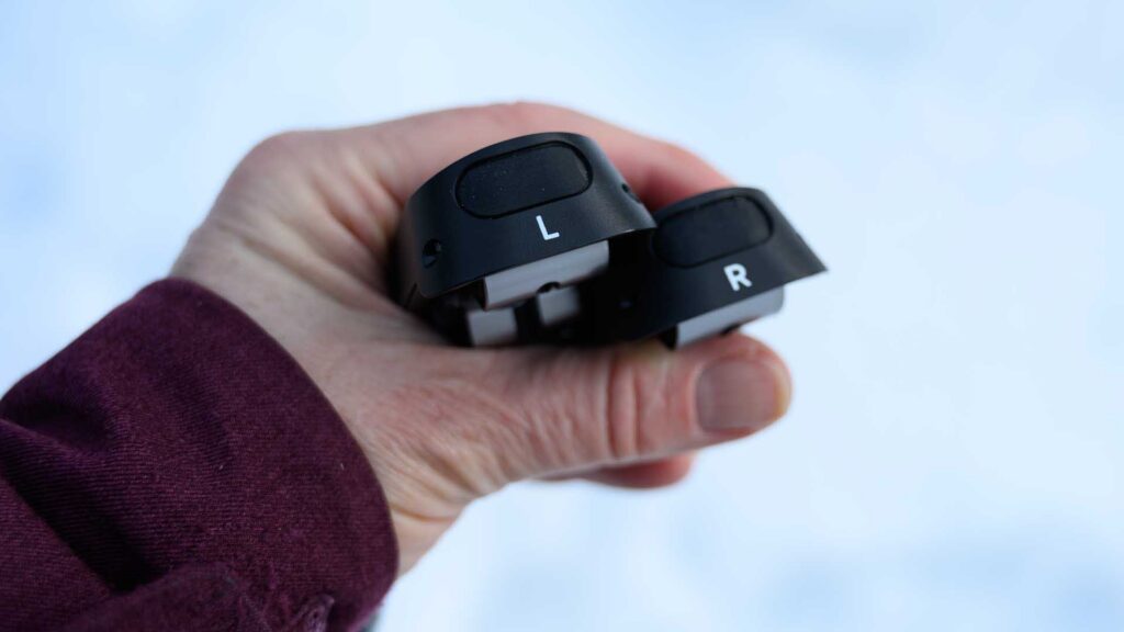 Woman's hand holding two Carv foot sensors labeled “L” and “R,” shown from the top against a snowy background.