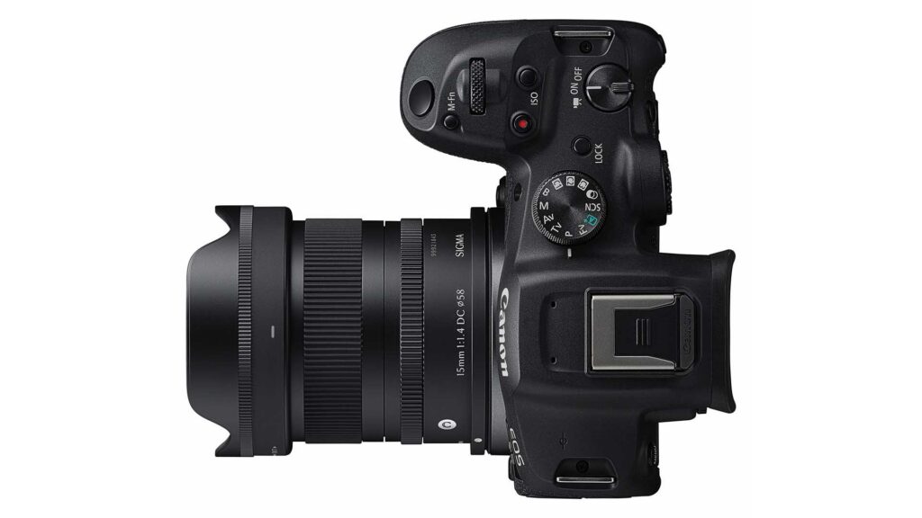 Top-down view of a Canon EOS camera fitted with a Sigma 15mm F1.4 DC Ø58 lens and petal-shaped hood. Lens barrel text reads “15mm 1:1.4 DC Ø58” and “SIGMA,” with the camera’s mode dial and hot shoe visible.