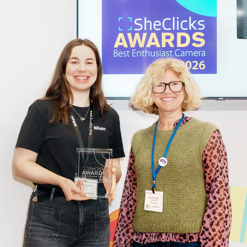 Two women posing with an award; backdrop reads “SheClicks Awards Best Enthusiast Camera 2026.”