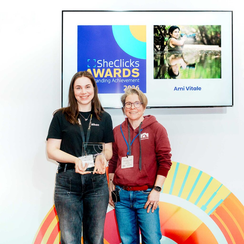 Two women posing with an award; screen reads “SheClicks Awards Outstanding Achievement 2026” and “Ami Vitale.”