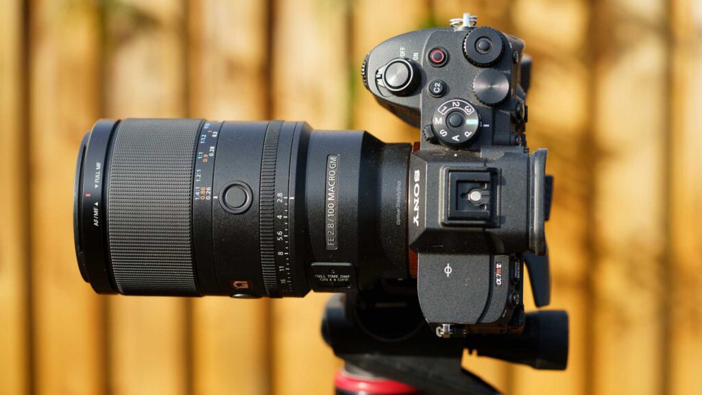 Top-down angle of Sony A7R V with Sony FE 100mm F2.8 Macro GM OSS attached, highlighting mode dial, shutter button, and hot shoe.