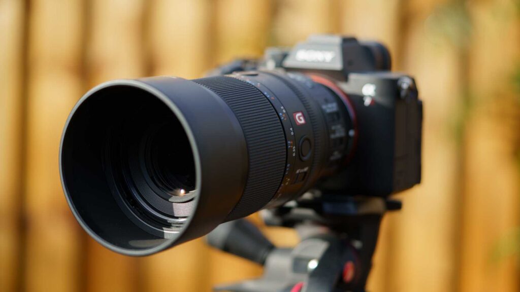 Front angled view of the macro lens mounted on camera with lens hood attached, emphasizing large front element and shallow depth of field.