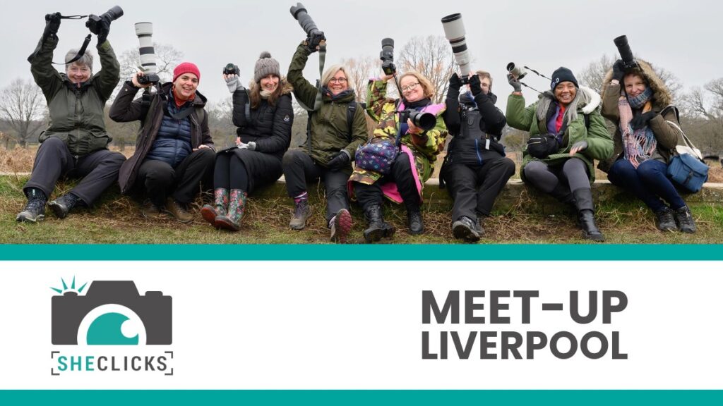 Group of women photographers holding cameras outdoors; banner below reads “SheClicks Meet-Up Liverpool” with camera logo.