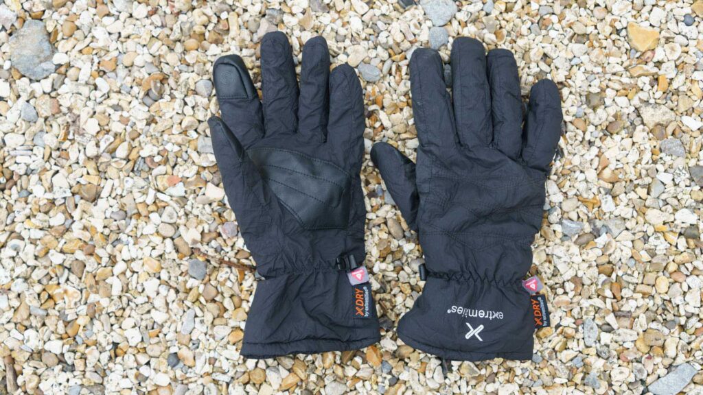 Pair of black Extremities gloves laid flat on small pebbles, showing palm and back design.