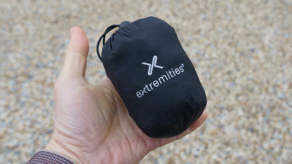 Compact black drawstring pouch with Extremities logo held in a hand against a pebbled background.
