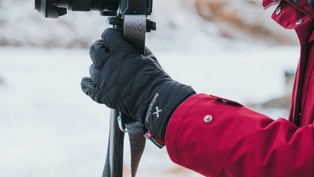 Close-up of a gloved hand gripping a camera strap attached to a camera, with a snowy background.