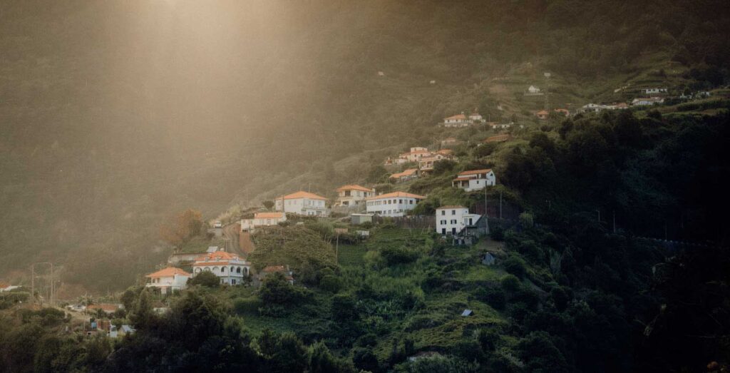 Hillside village with white houses and red roofs scattered across green mountains under soft golden haze