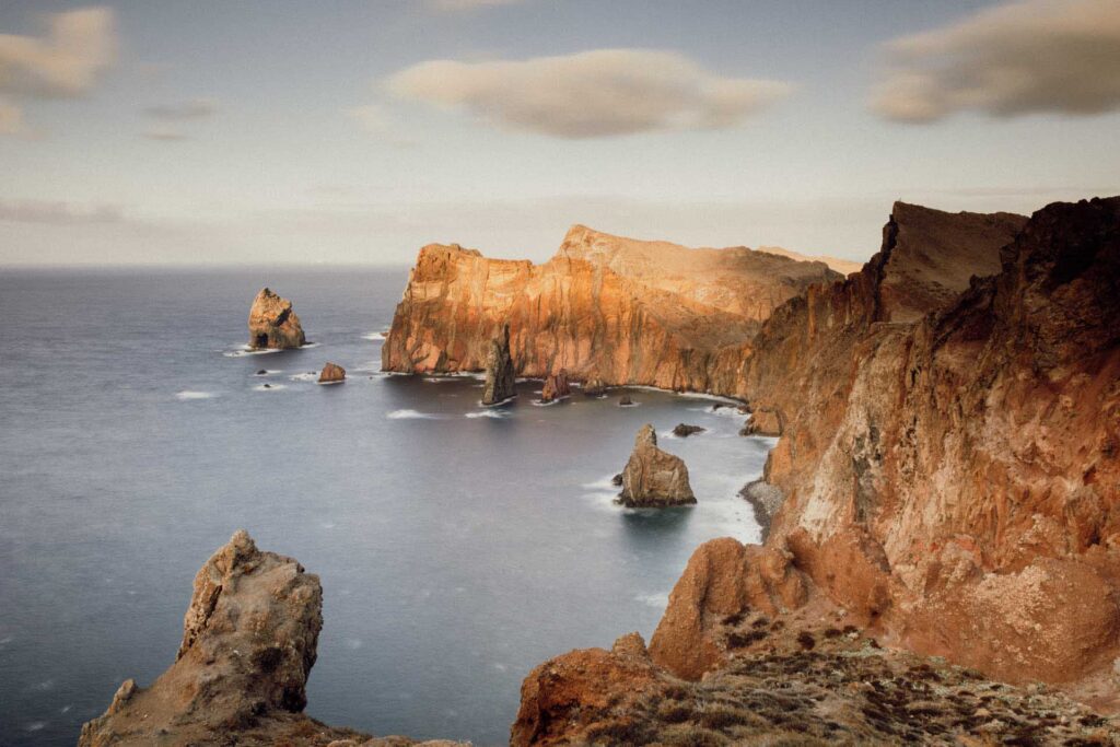 Rugged coastal cliffs with tall rock formations rising from calm ocean under partly cloudy sky