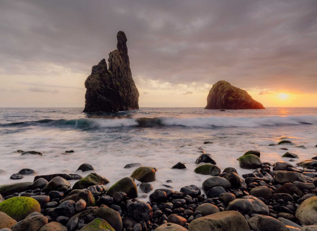 Rocky beach with waves rolling in and two large sea stacks at sunset