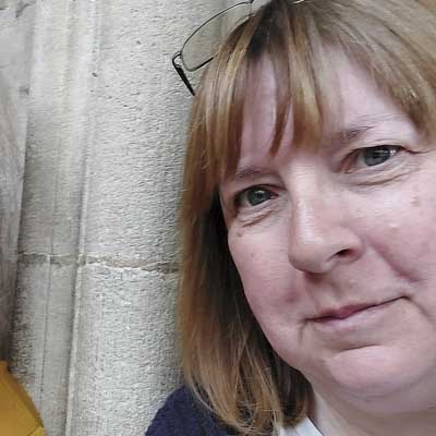 Close-up portrait of Vanessa Wheeler beside a stone wall, with glasses resting on her head.
