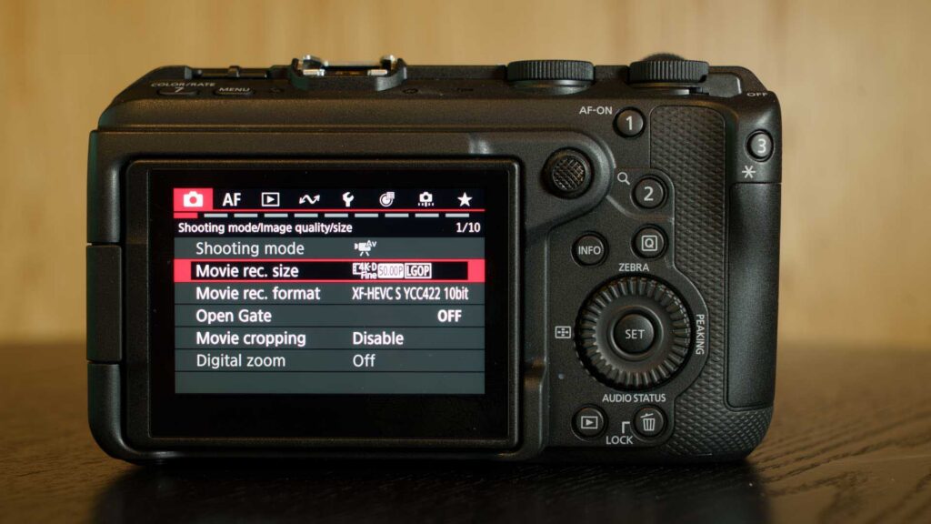 Rear view of the Canon EOS R6 V displaying the video recording settings menu on the LCD screen. Options shown include movie recording size, format, open gate, movie cropping, and digital zoom.
