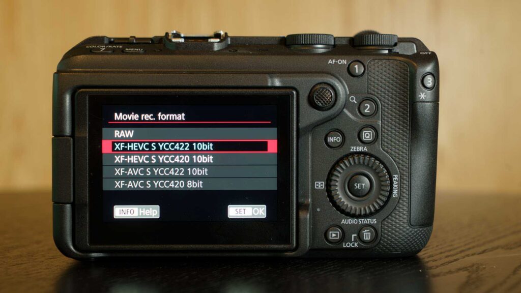 Rear LCD screen of the Canon EOS R6 V displaying video codec and color sampling options. XF-HEVC S YCC422 10bit is highlighted in the movie recording format menu.