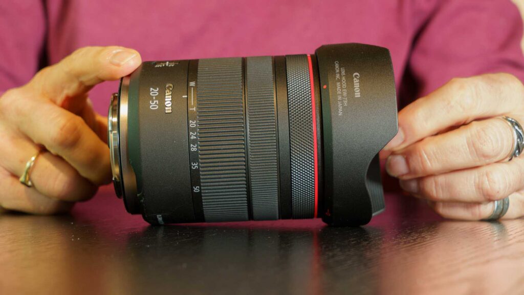Canon RF 20-50mm F4L IS USM PZ lens held between two hands, showing the compact size and lens hood design.