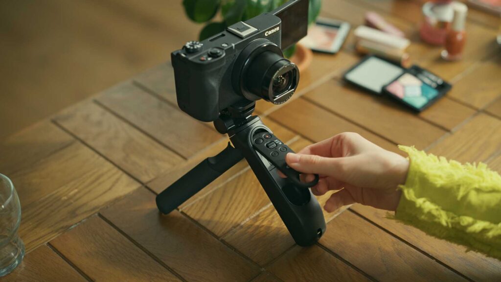 Canon HG-200TBR tripod grip with attached camera on a wooden table while a person presses controls on the built-in handle remote.