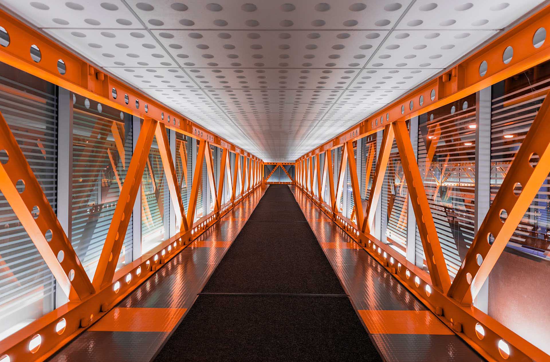 Symmetrical corridor with orange steel framework and geometric patterns.