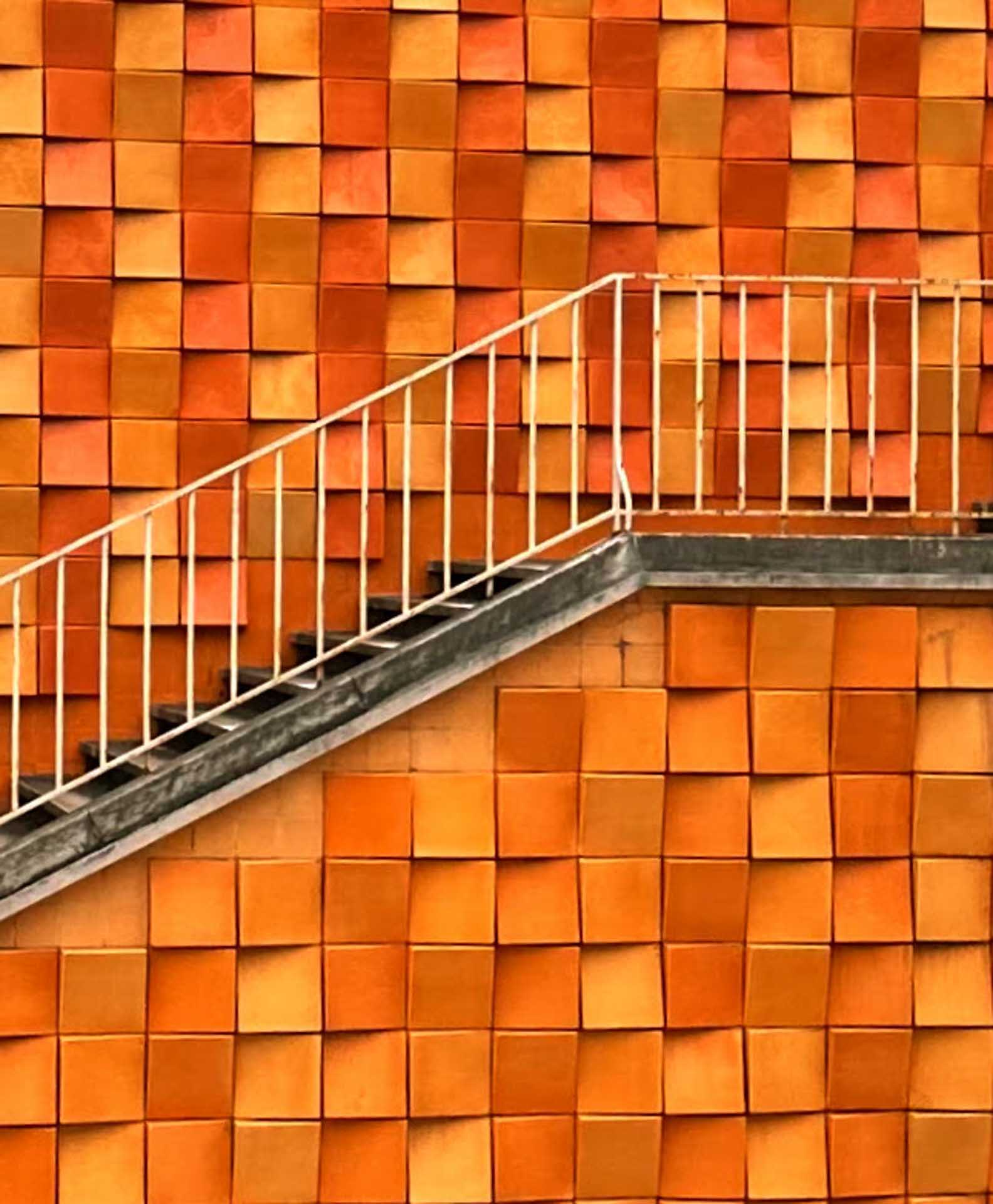 Diagonal staircase against a textured wall of orange tiles.