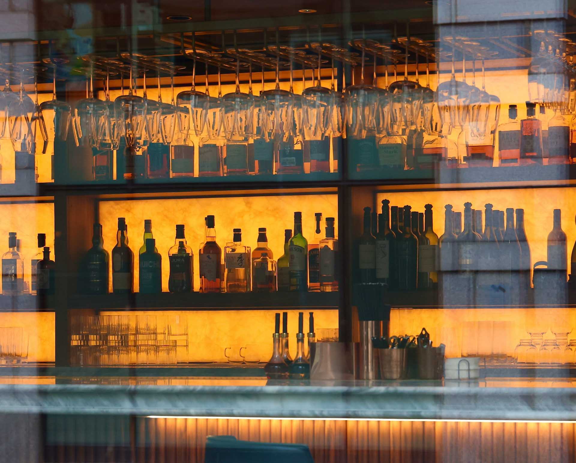 Backlit bar shelves with hanging glasses and bottles glowing in warm orange light.