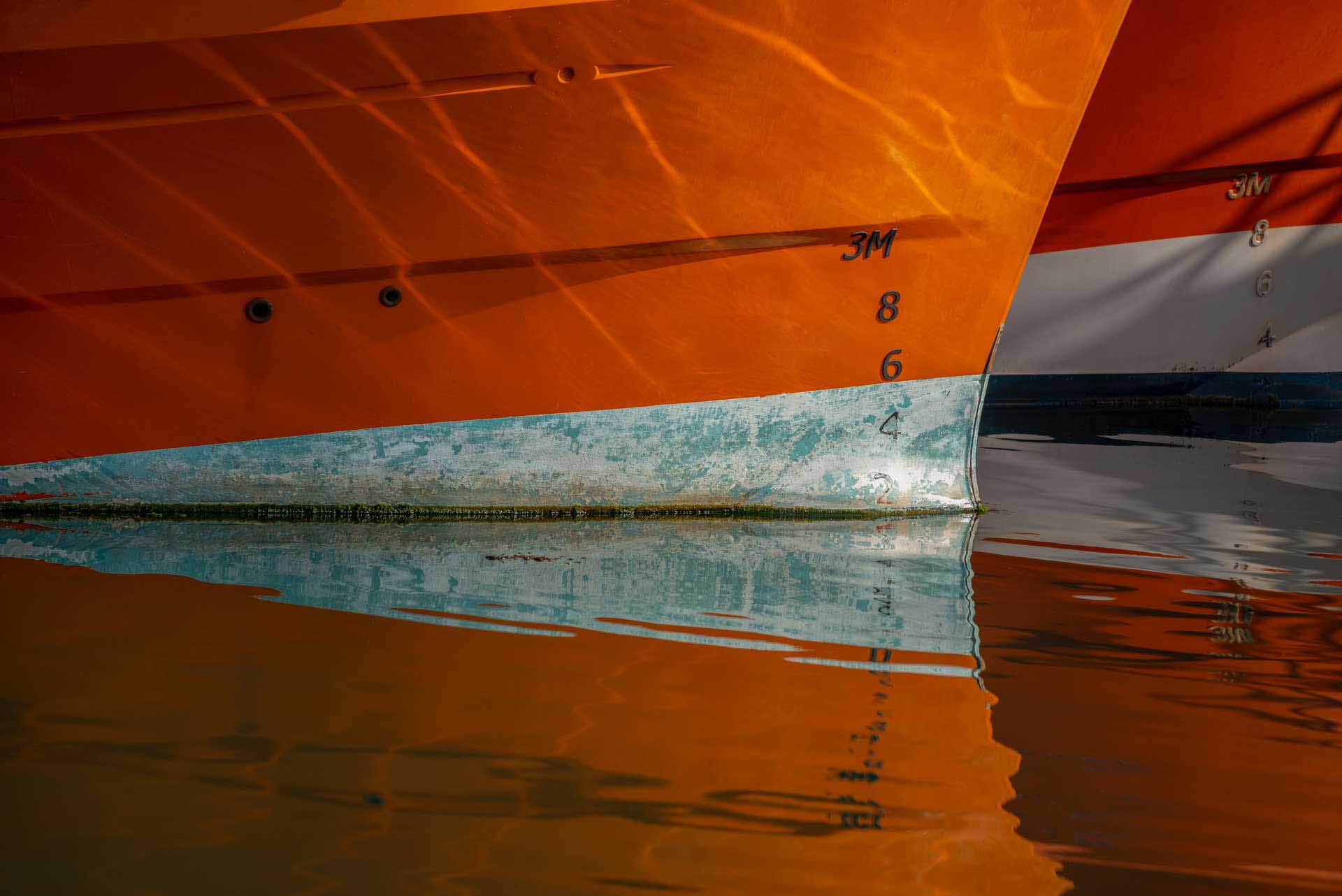 Close-up of an orange boat hull reflected in calm water.