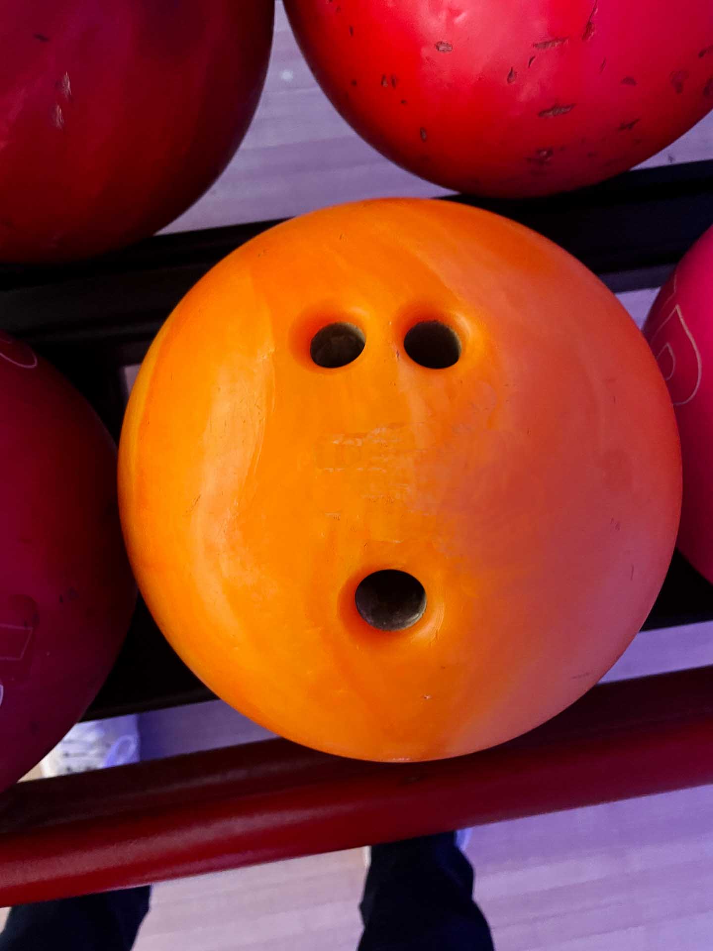 Orange bowling ball on a rack surrounded by red bowling balls.