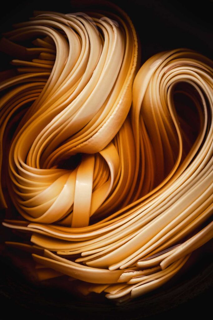 Close-up of folded ribbons of fresh pasta coiled together in warm golden light.