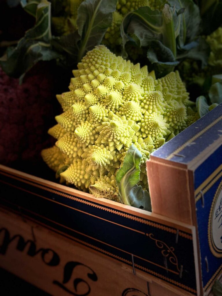 Romanesco cauliflower with spiral florets displayed in a wooden produce crate.
