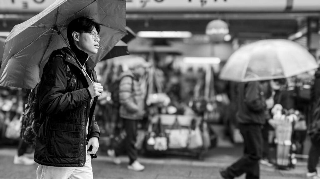 Person holding an umbrella while walking through a rainy city street, with pedestrians blurred in the background.