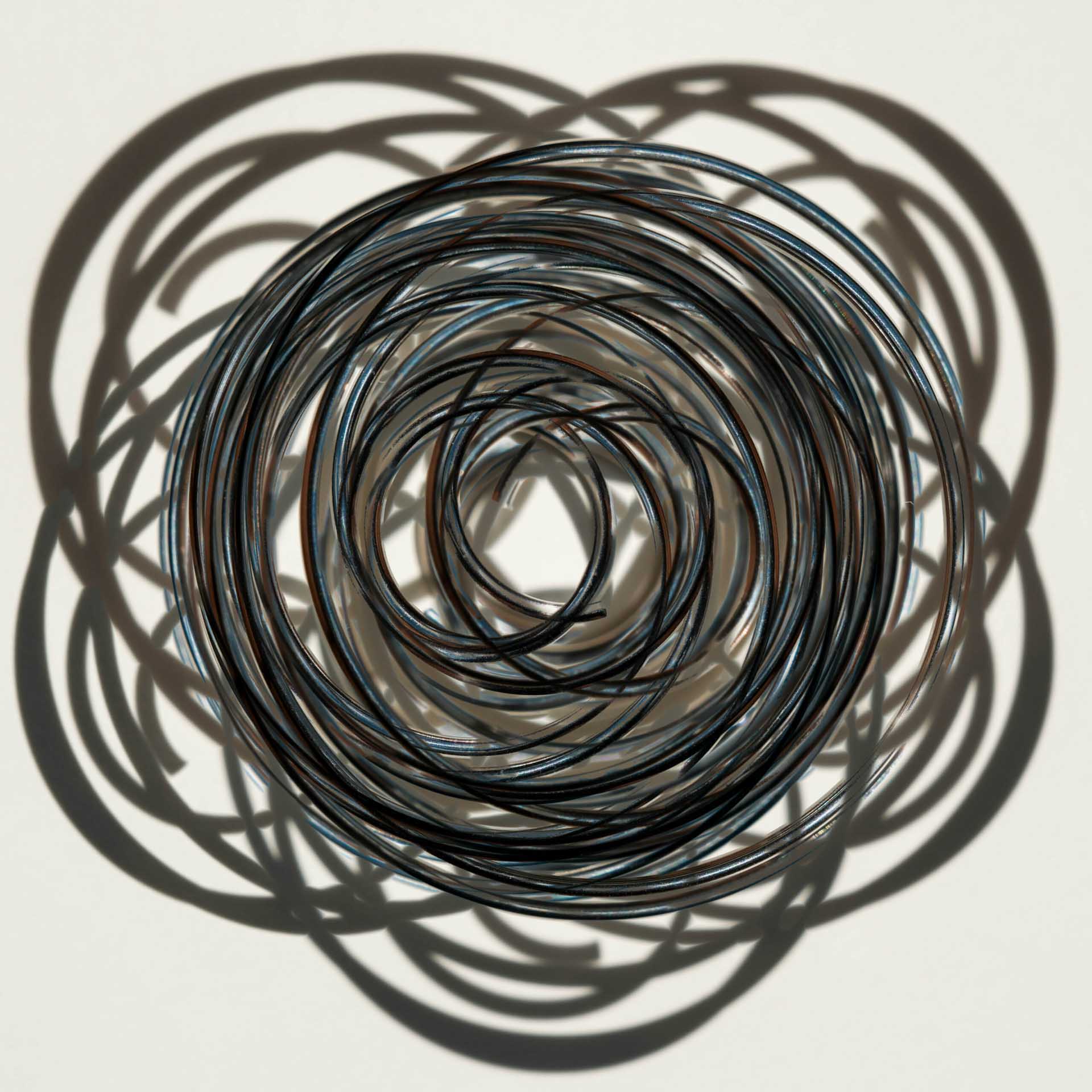 Coiled wire arranged in concentric circles casting overlapping shadows on a white surface.