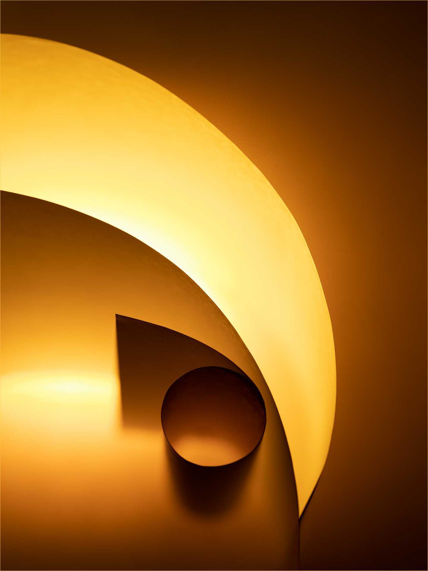 Abstract study of curved shapes and shadows created by a glowing orange lamp.