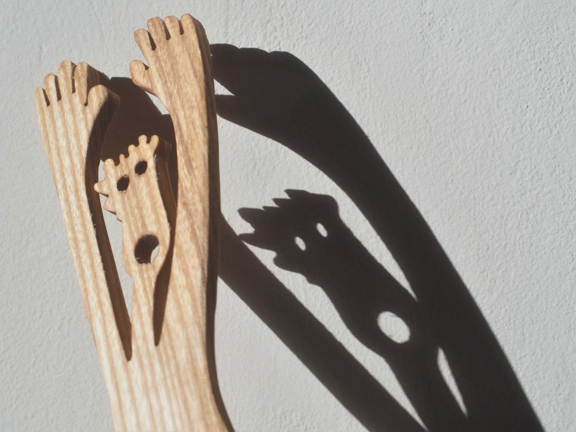 Wooden kitchen utensils and their elongated shadows creating playful shapes on a white wall.