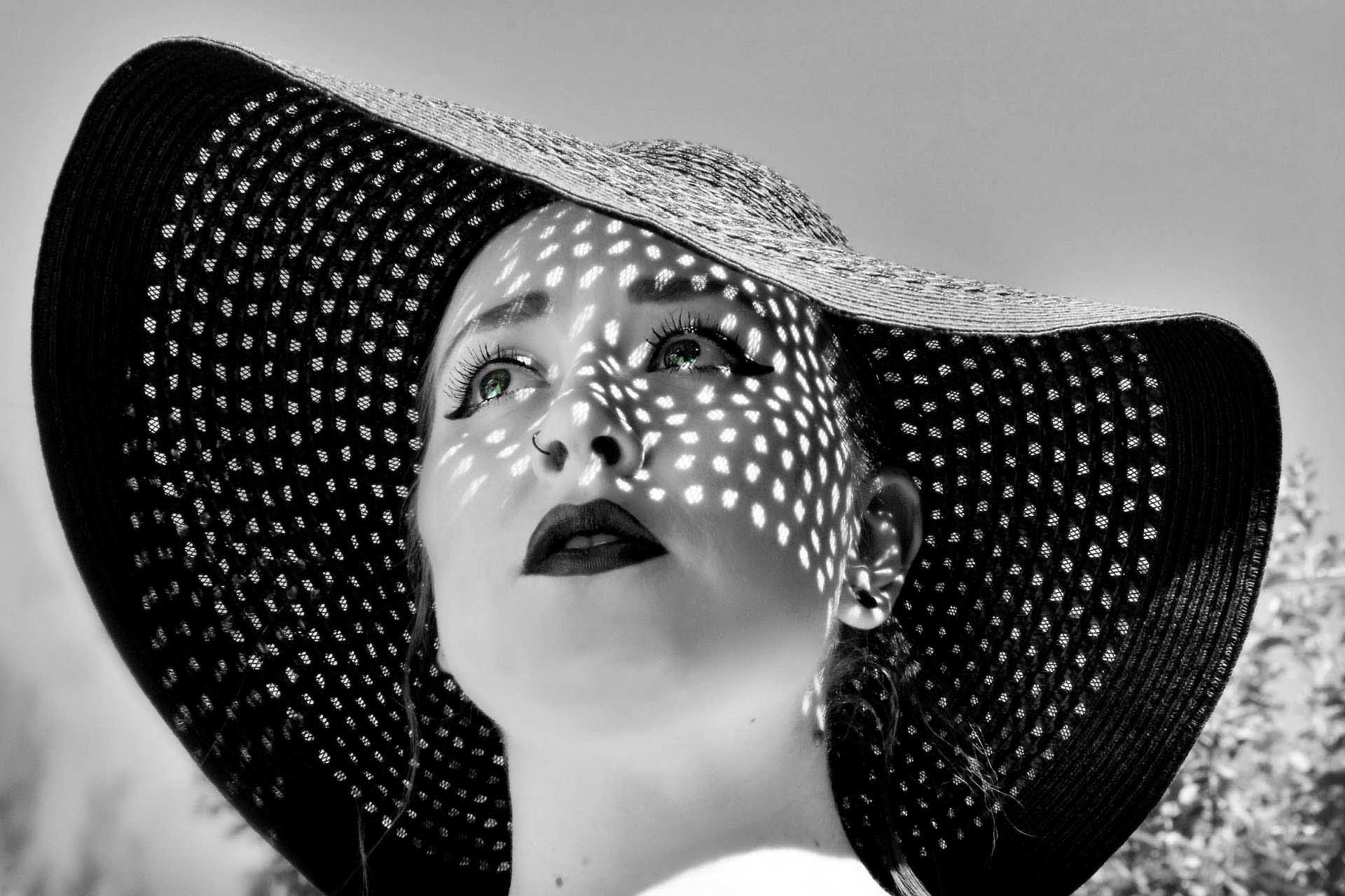 Portrait of a woman wearing a wide-brimmed hat with dappled light and shadow patterns across her face.