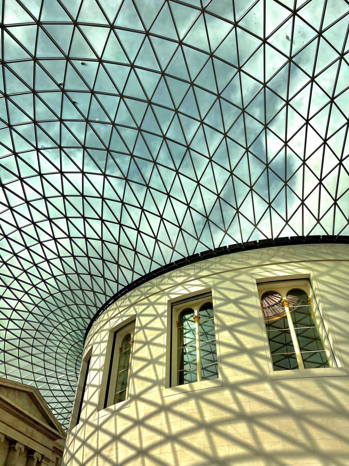 Patterned shadows from a glass roof falling across the curved facade of a museum building.