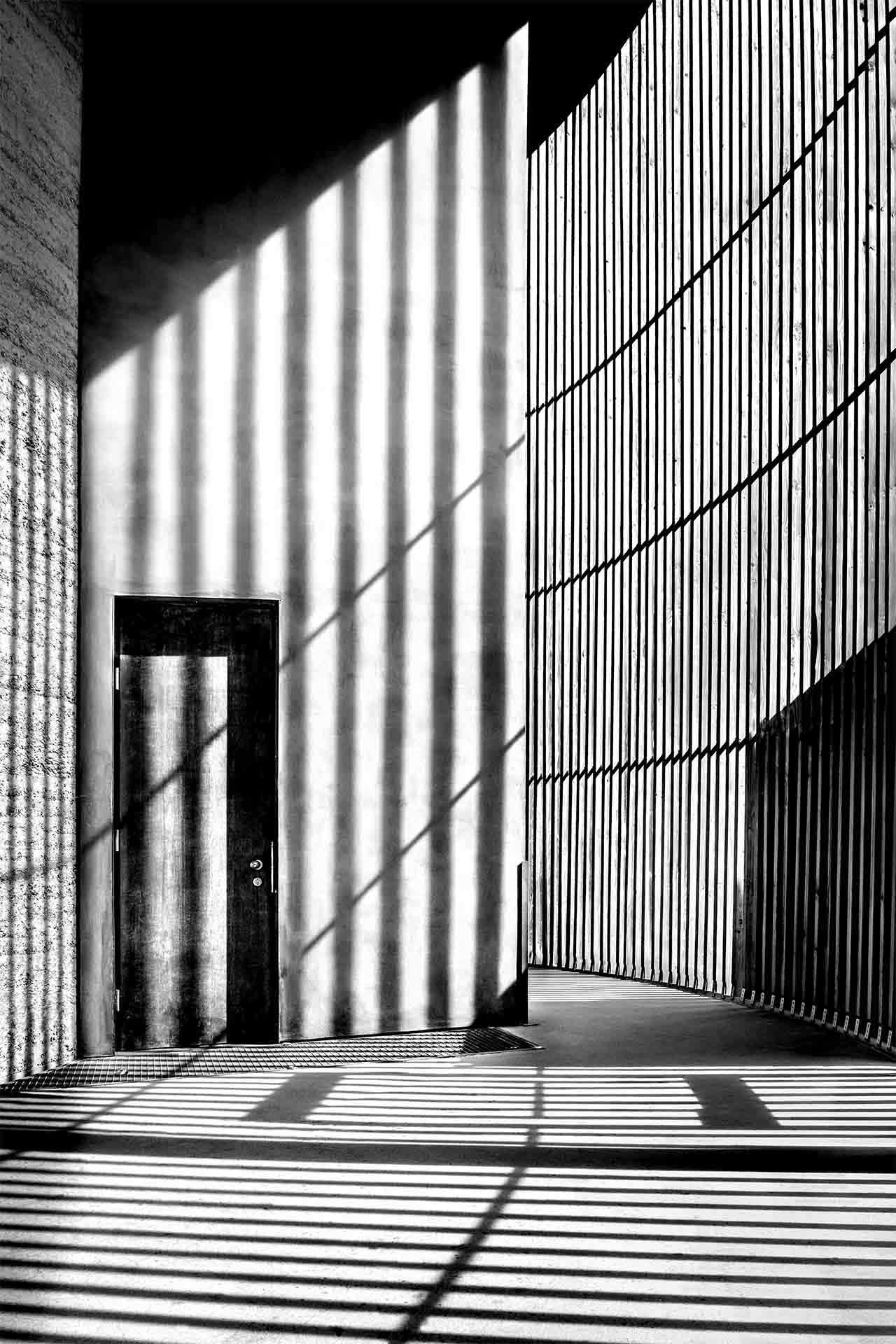 Black and white scene of striped shadows and curved walls creating an abstract architectural composition.