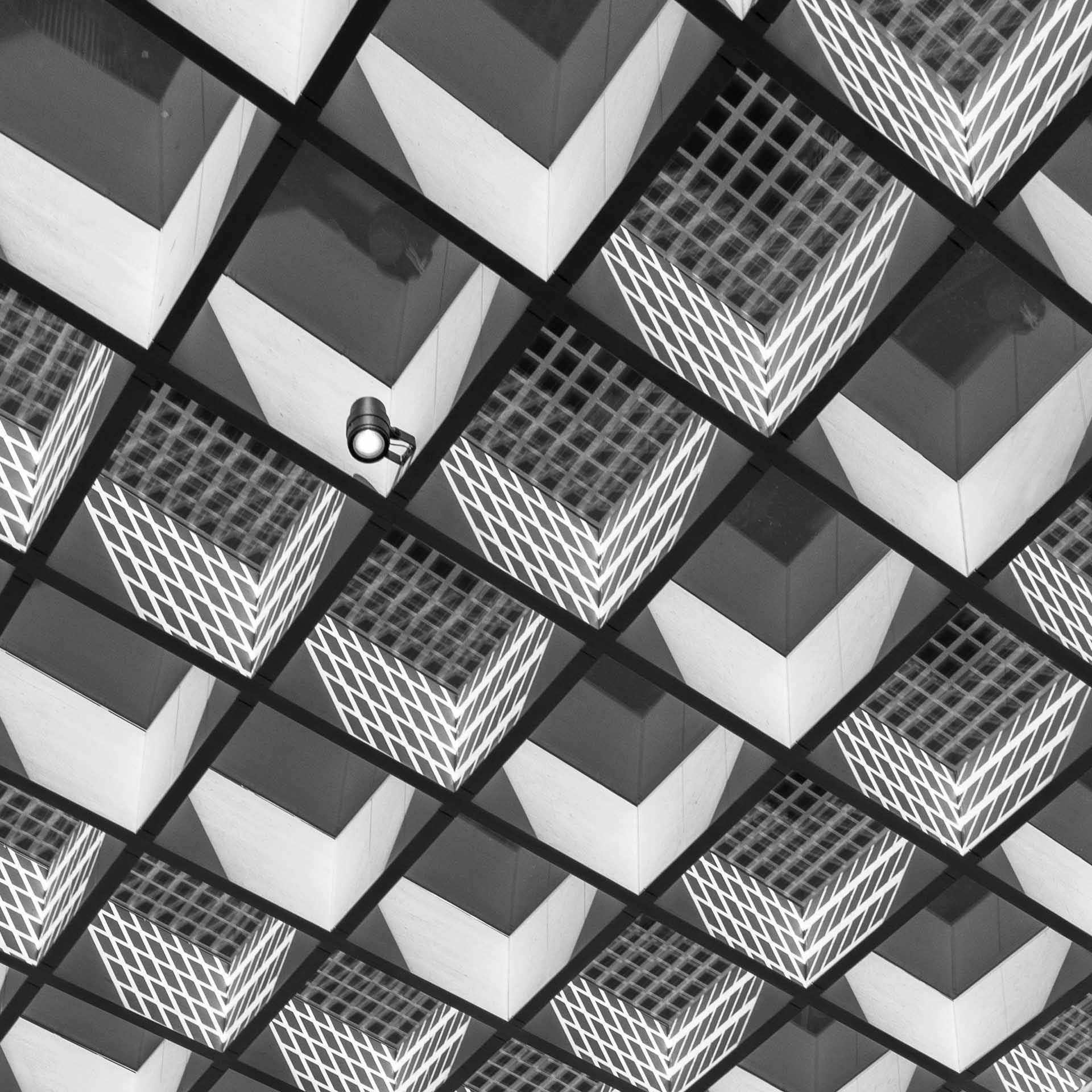 Black and white geometric ceiling pattern with a single security camera among repeating shapes.