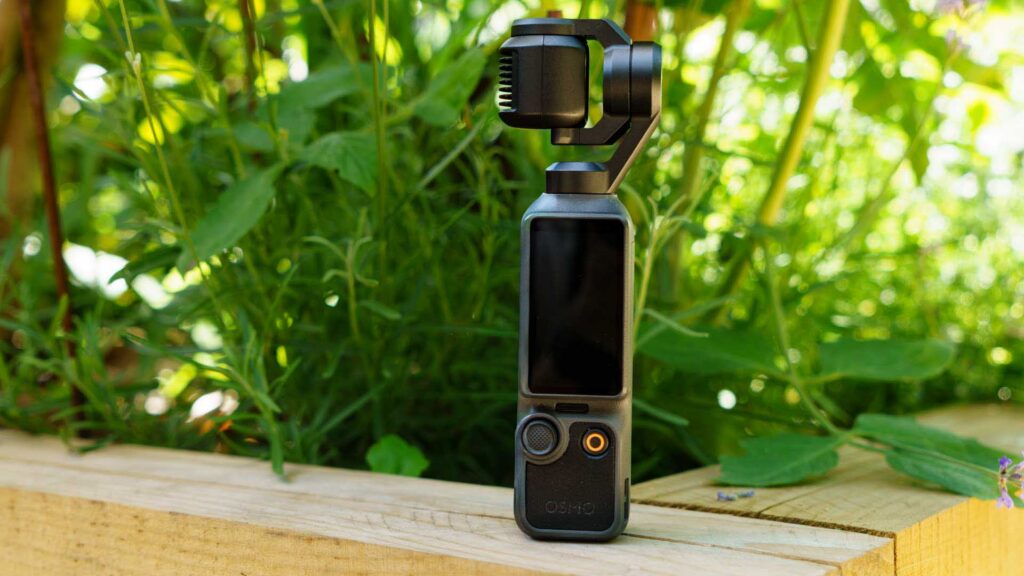 Front view of a DJI Osmo Pocket 4 standing upright on a wooden surface with its screen turned off.