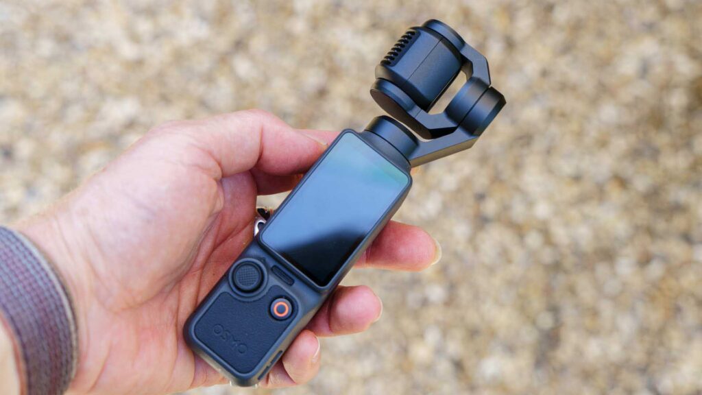 Hand holding a DJI Osmo Pocket 4, highlighting the compact design, touchscreen, and gimbal-mounted camera.