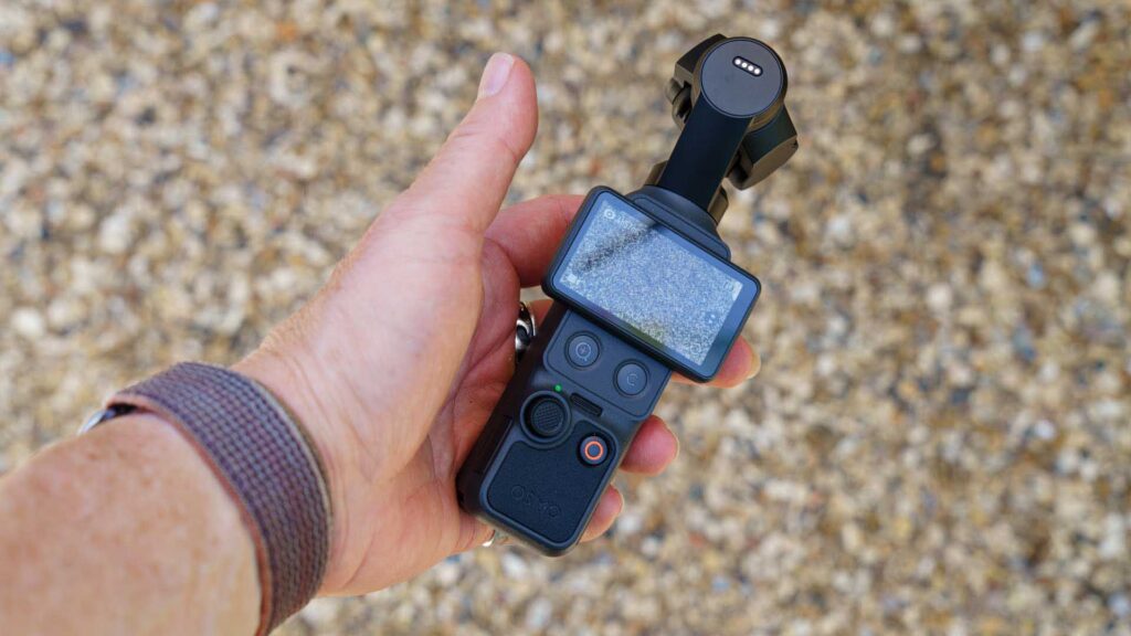 DJI Osmo Pocket 4 held in one hand with the touchscreen flipped outward, showing camera controls and status indicators.