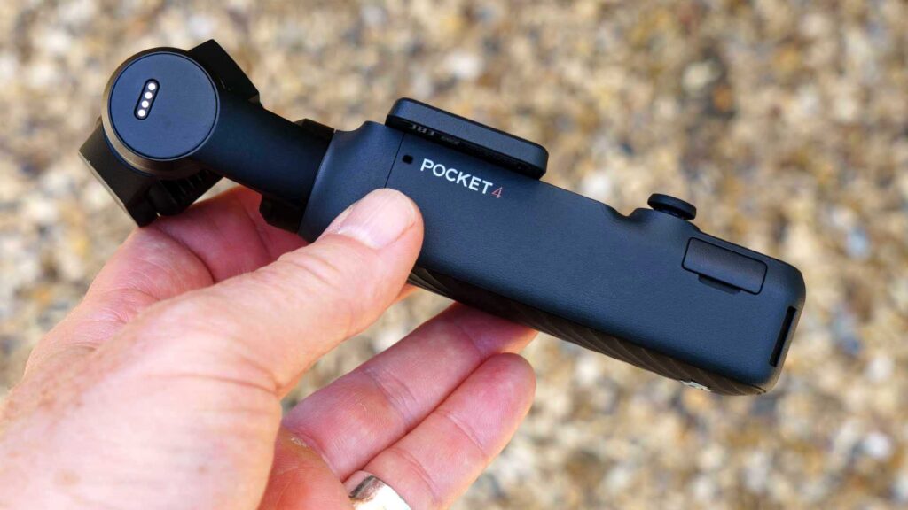 Side view of a DJI Osmo Pocket 4 in hand, with the product name “POCKET 4” visible on the device body.