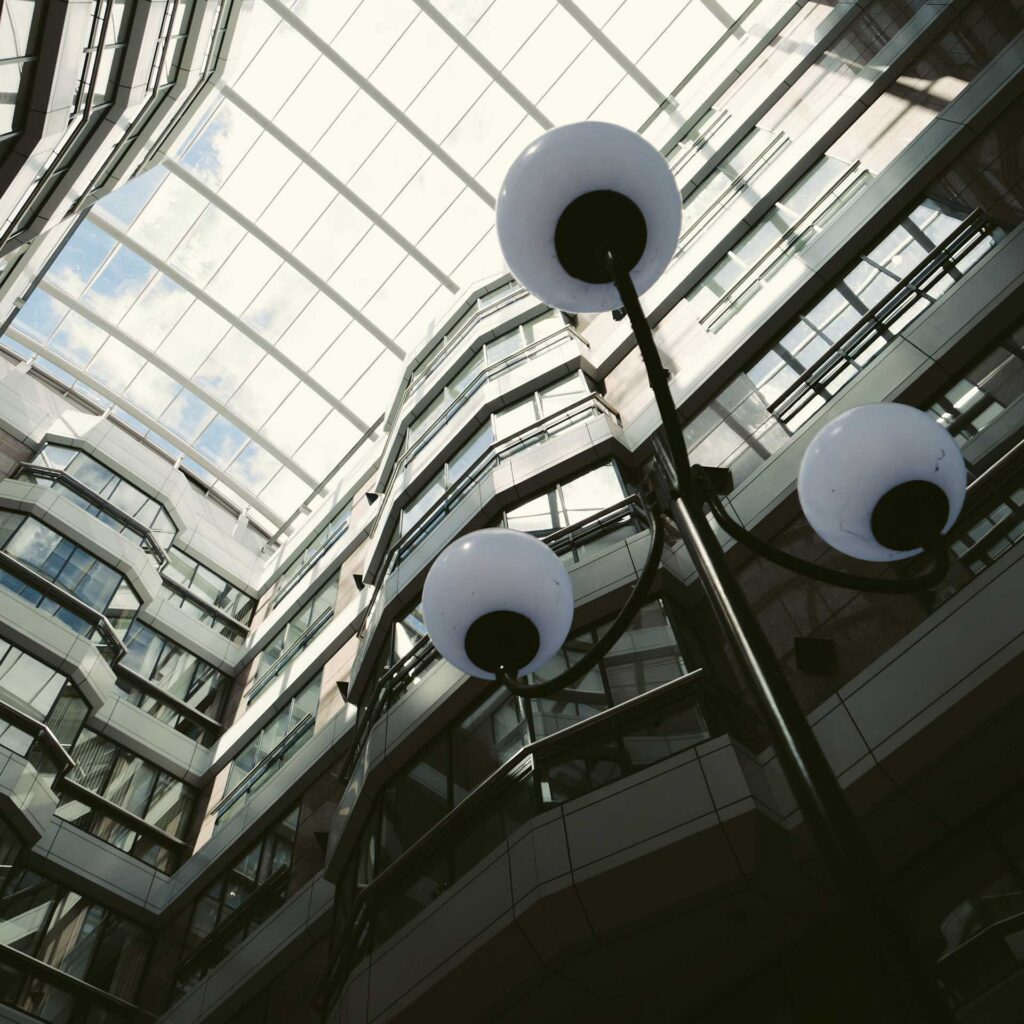 Interior atrium viewed from below, featuring a glass roof, angular balconies, and globe-topped light fixtures.