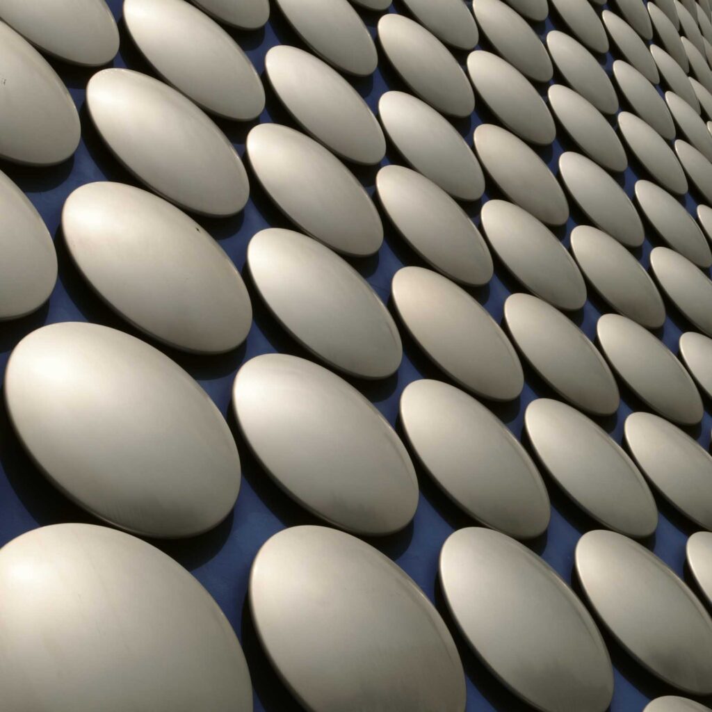 Close-up pattern of silver circular façade panels casting soft shadows across a dark blue surface.