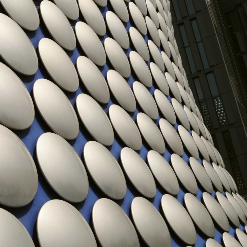 Diagonal view of a building façade clad in rows of silver circular discs, with dark windows visible at the edge.