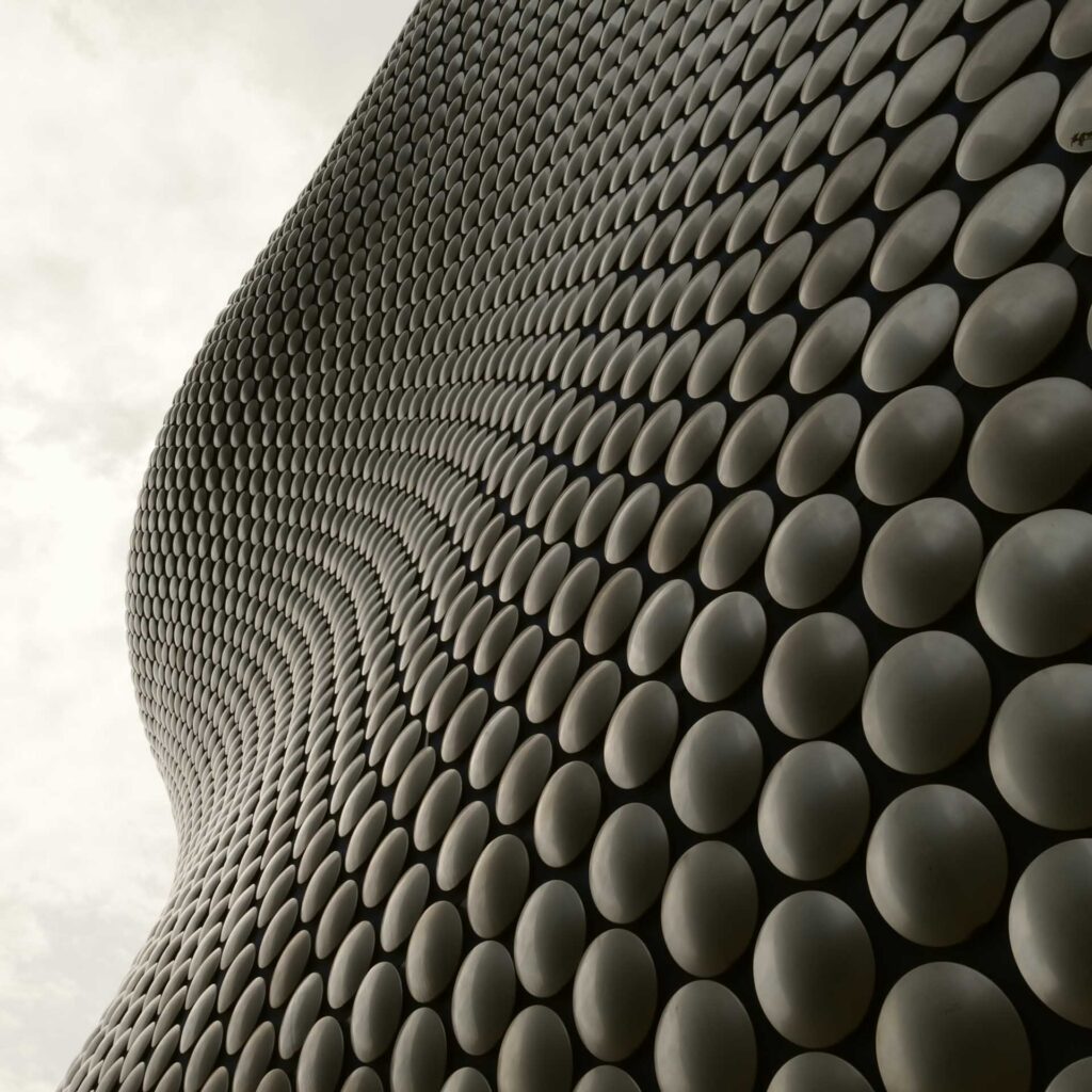 Curved metallic façade covered in circular discs, photographed from below to emphasize its sculptural form.