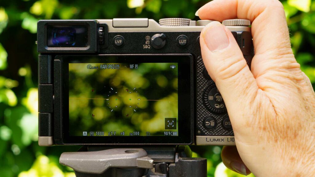 Hand adjusting the top control dial of the Panasonic Lumix L10 while the live view display is active.