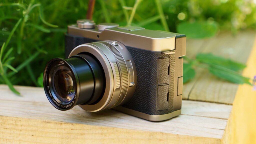 Three-quarter front view of the Panasonic Lumix L10 resting on a wooden surface outdoors, with the lens extended.